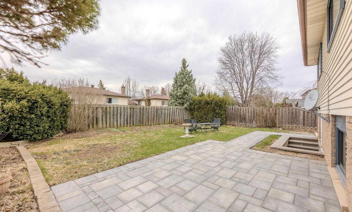 Backyard patio with stone pavers, lawn, wooden fence, shrubs, and leafless trees