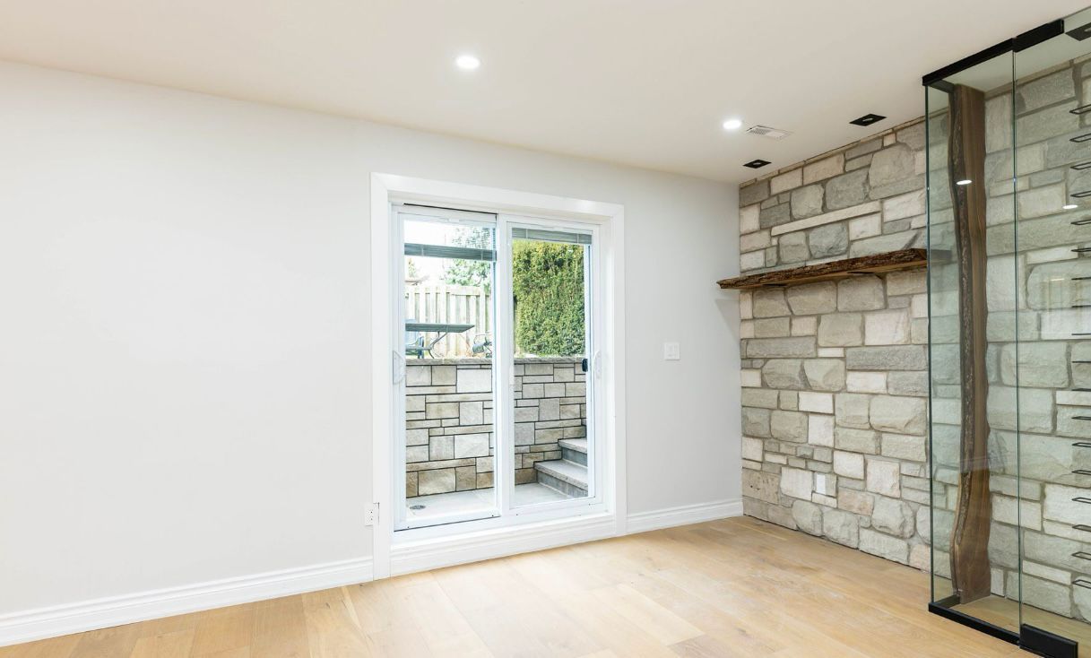 Empty modern room with light wood floors, white walls, and a stone accent wall beside a glass door.