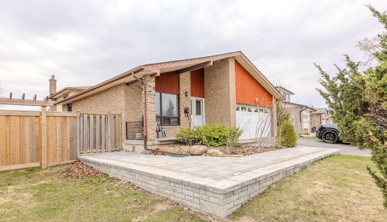 Single-story brick house with a fenced yard, paved patio, and orange accents