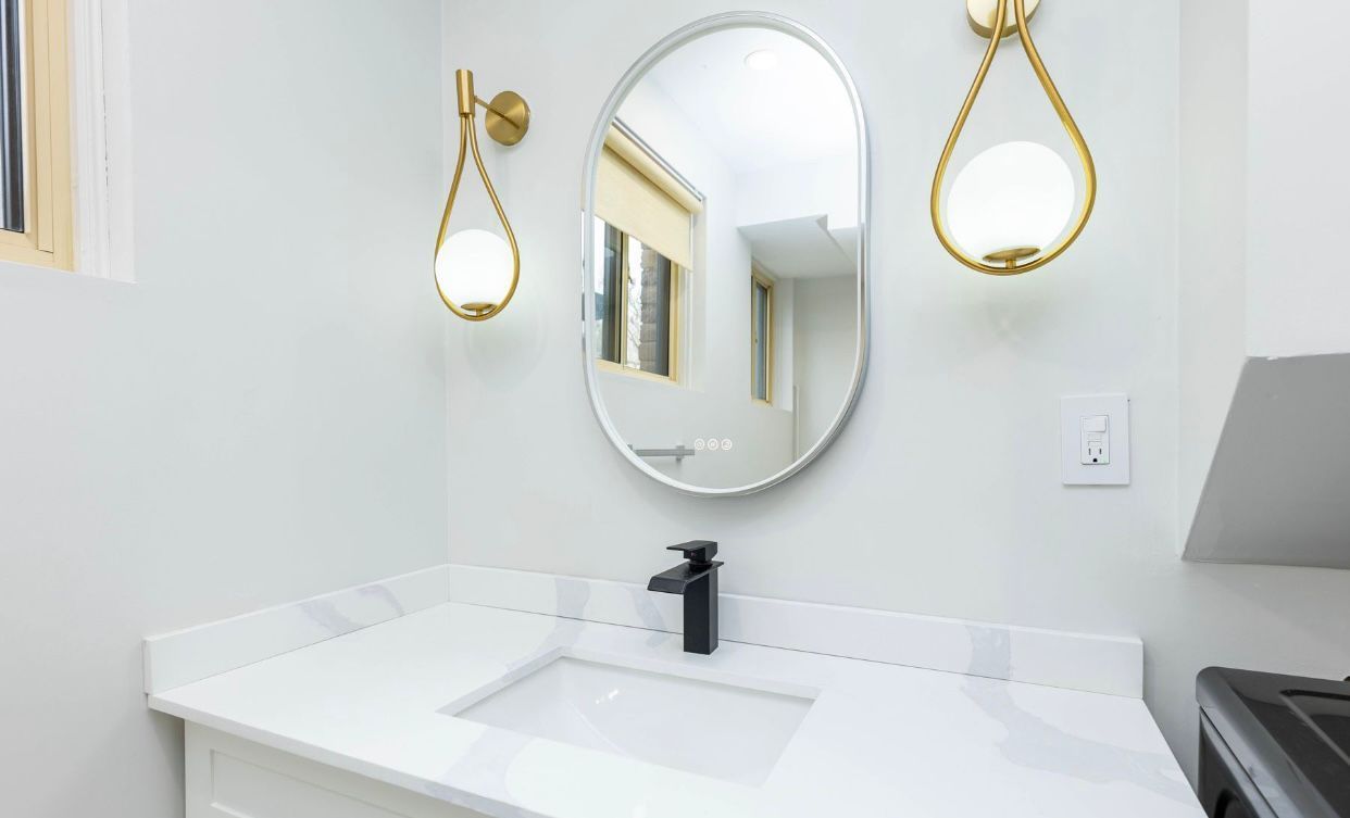 Modern white bathroom vanity with oval mirror, gold sconces, and black faucet