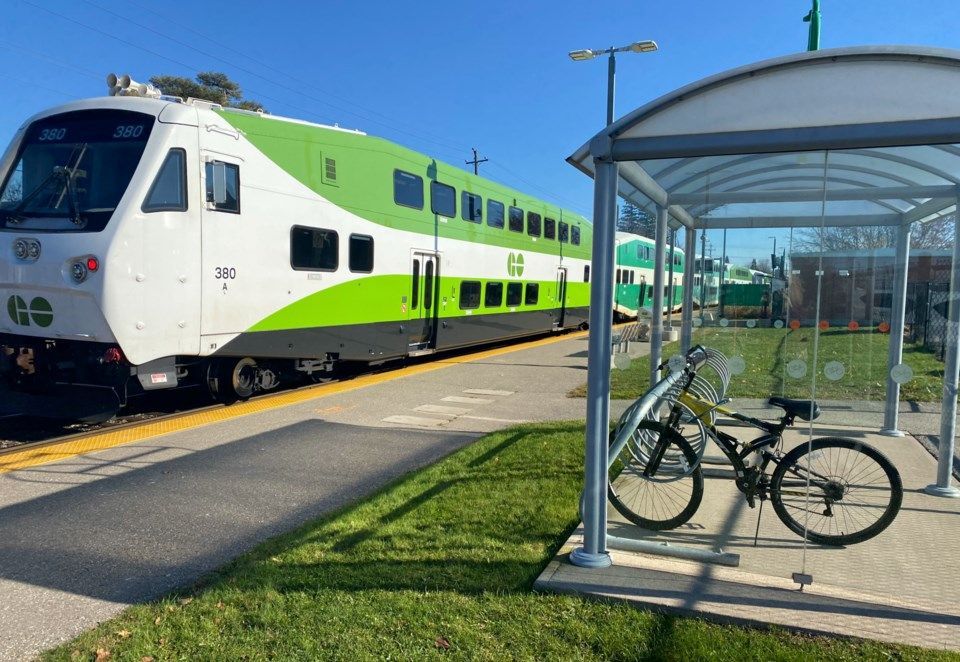 Green and white train at a station platform beside a bike shelter with bicycles.