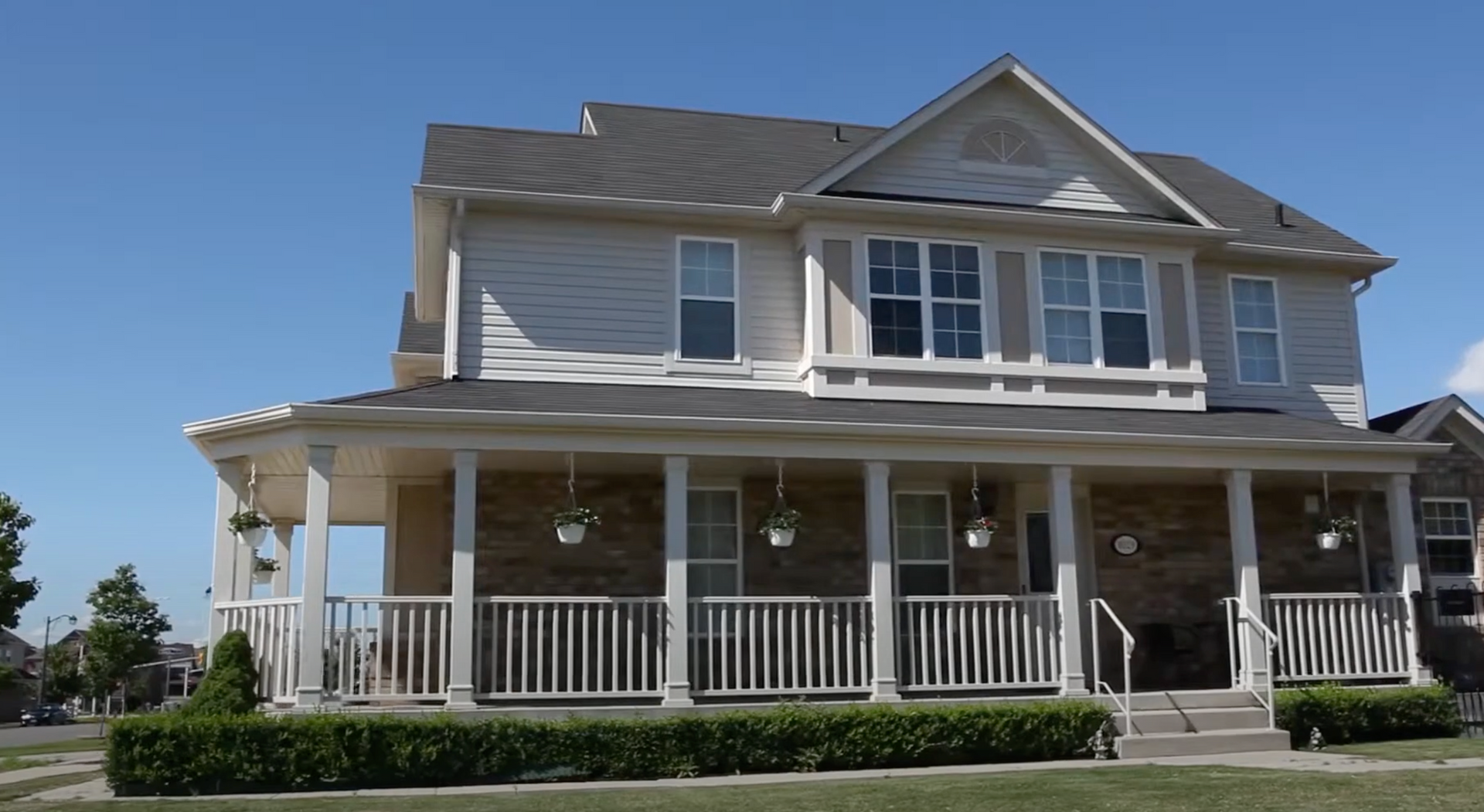Two-story suburban house with white porch columns and beige siding under a clear blue sky