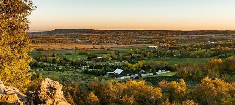 Autumn landscape with golden trees, green fields, and a wide valley under a warm sunset sky