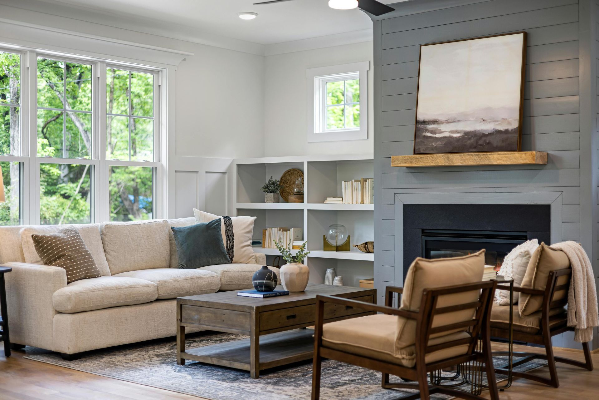 Living room with a beige sectional, fireplace, built-in shelving, and large windows.