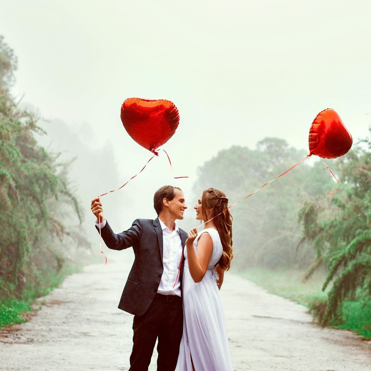 A bride and groom are holding red heart shaped balloons