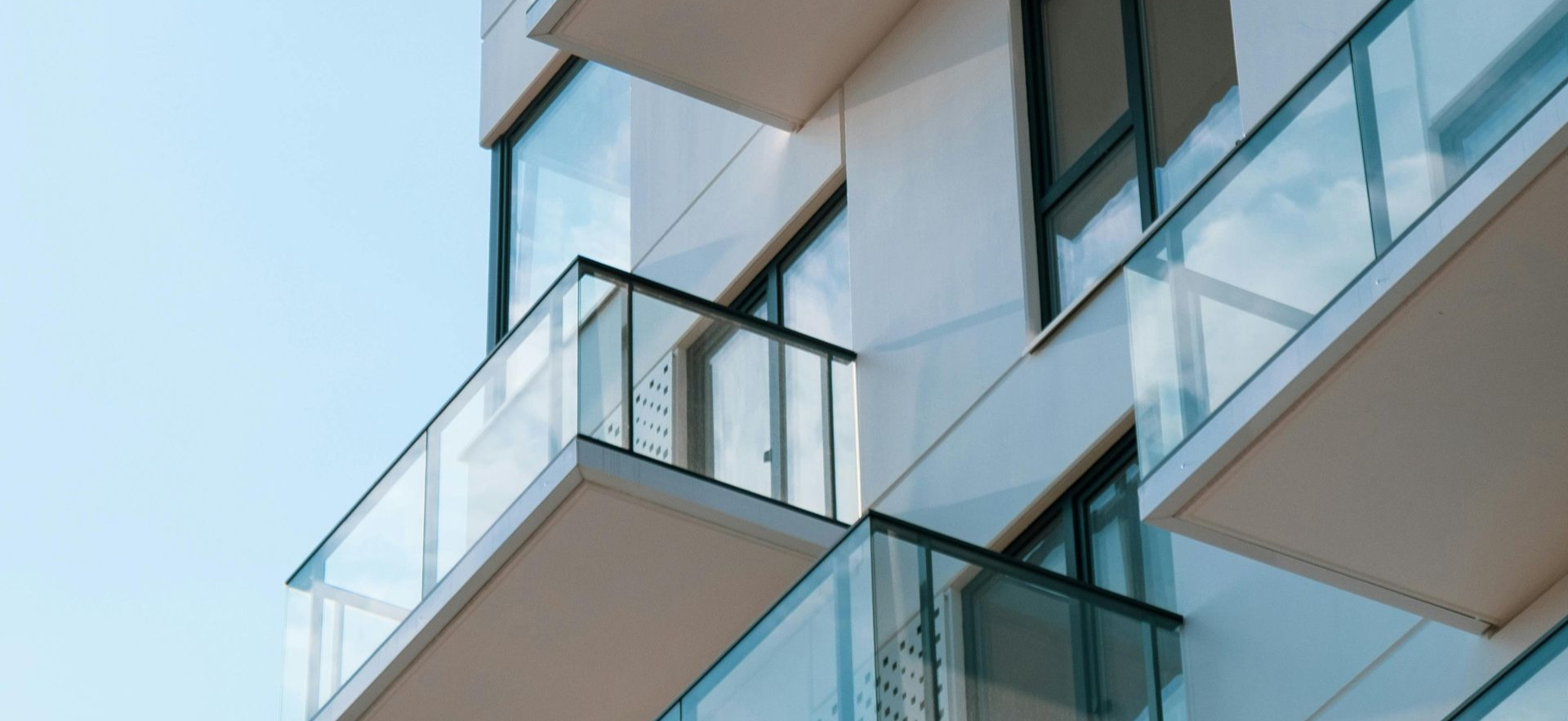 Modern apartment balconies with glass railings against a blue sky