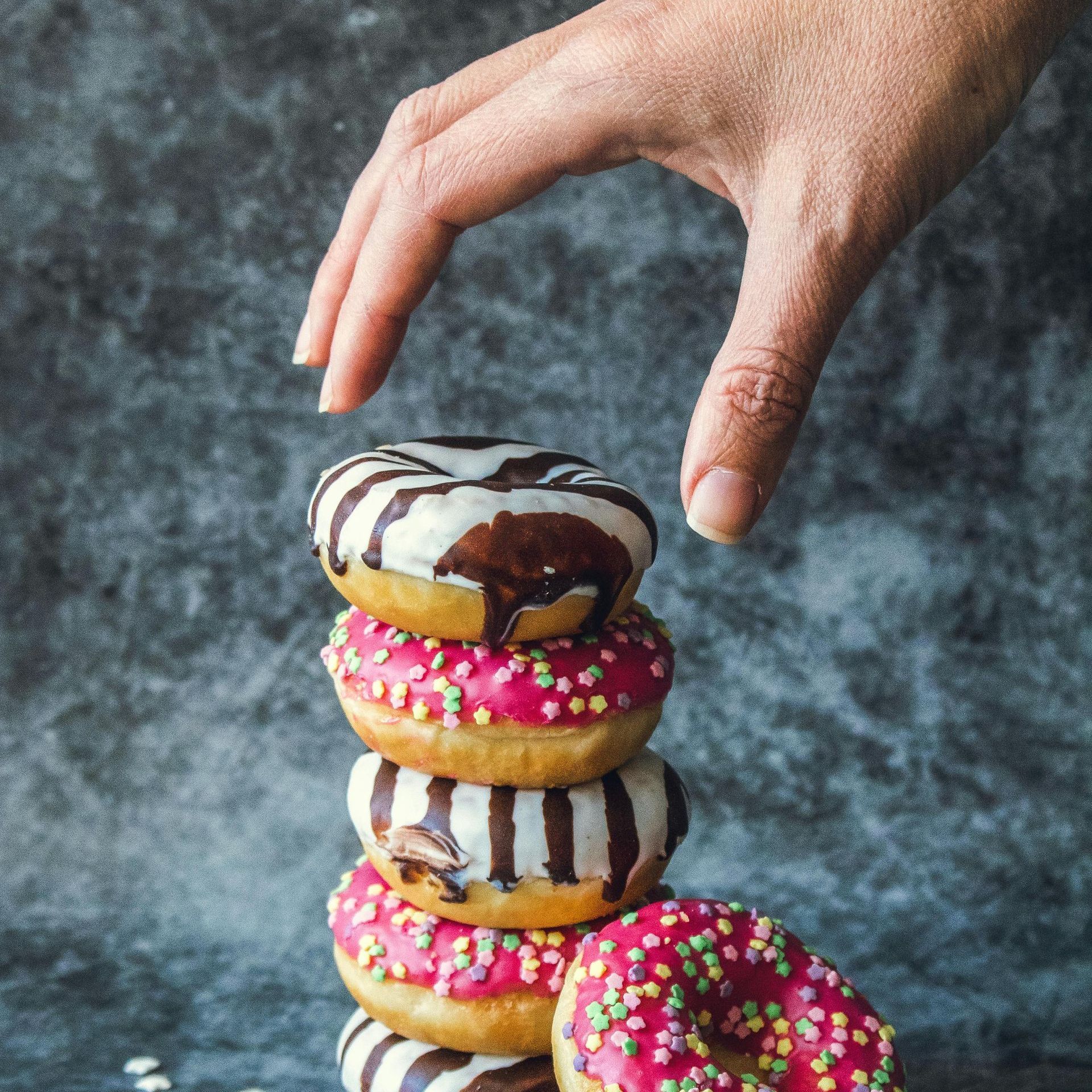 A hand is reaching for a donut on top of a stack of donuts