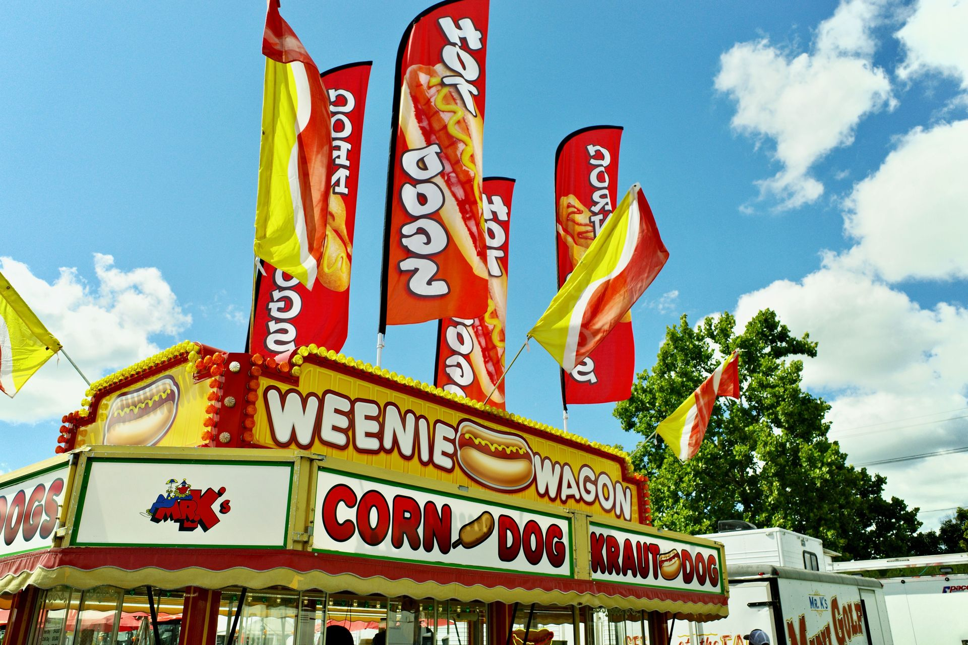 Carnival food stand with red flags and sign reading “WEENIE WAGON CORN DOG”