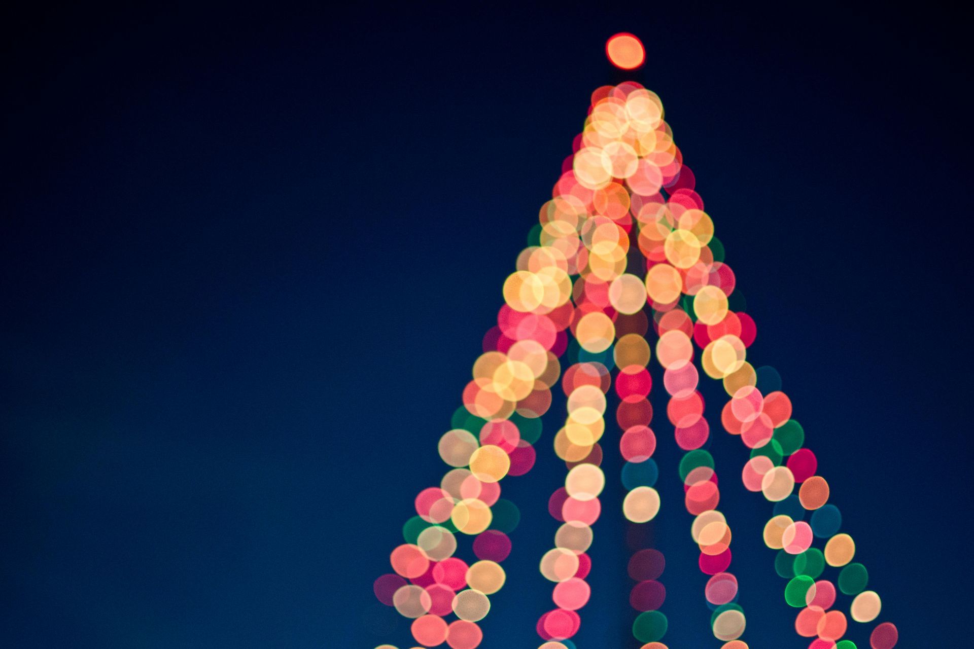 Christmas tree shape formed by colorful, blurred lights against a dark blue sky.