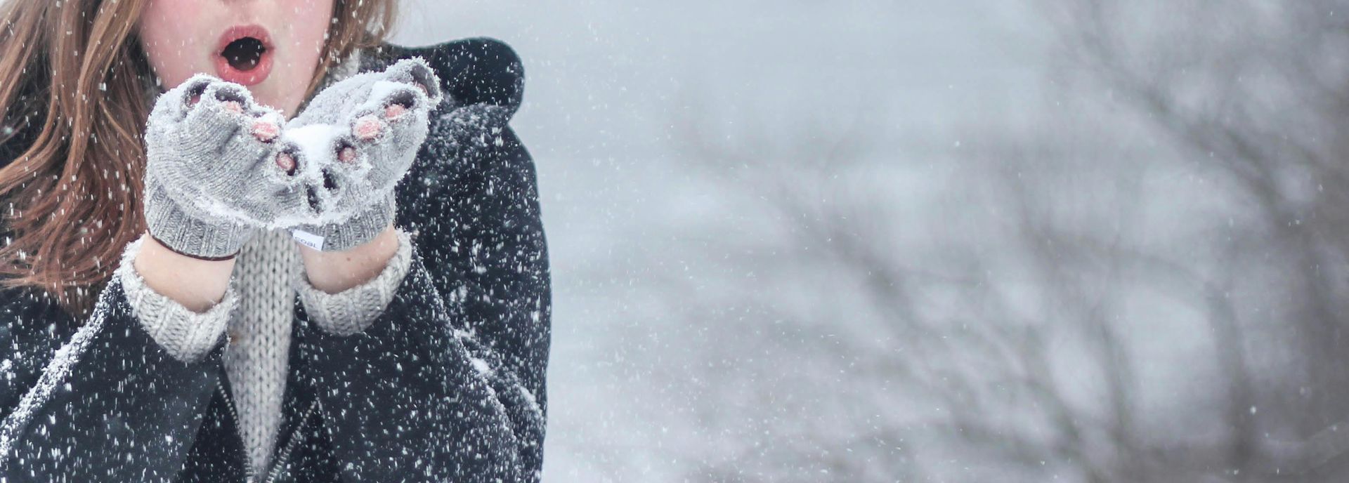 A woman is blowing snow from her hands in the snow.