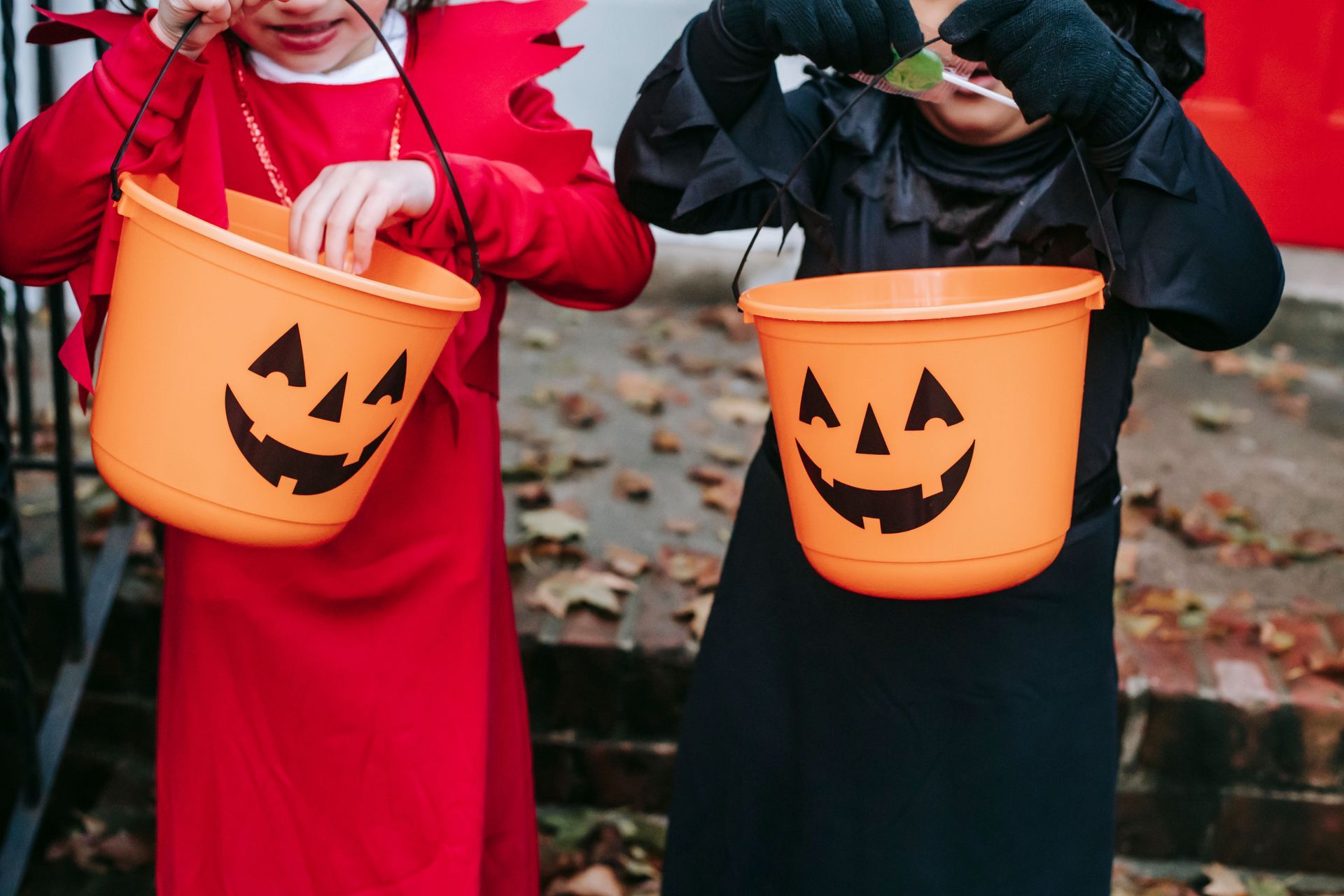 Two children in costumes holding orange jack-o'-lantern buckets for trick-or-treating.