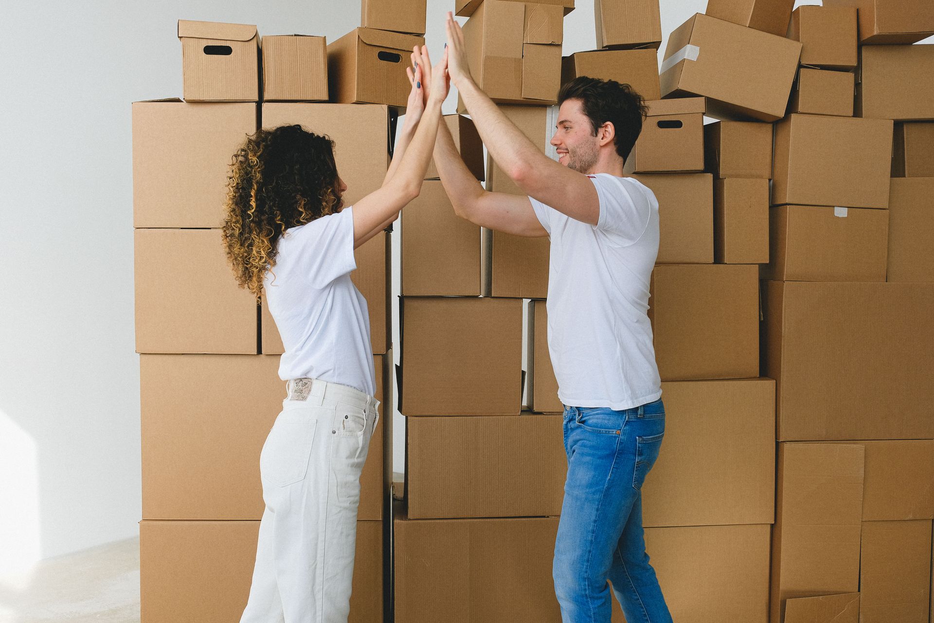Two people high-five in front of a wall of stacked cardboard moving boxes.