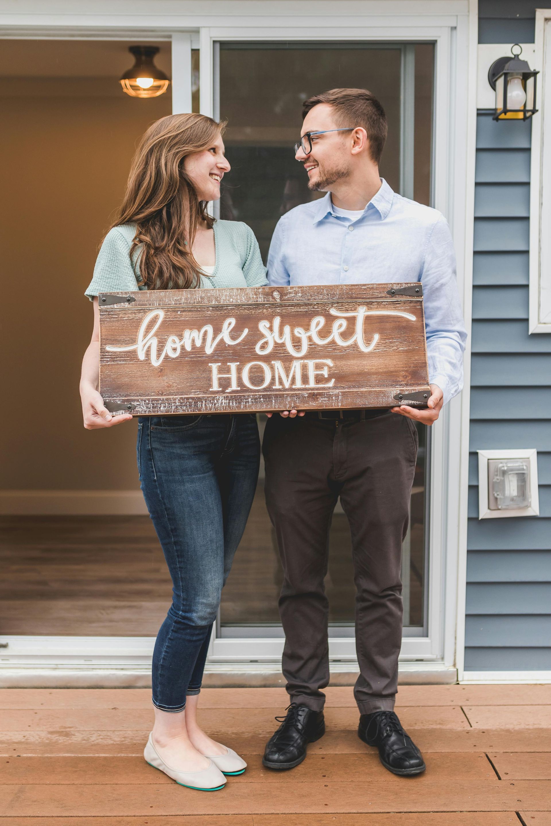 A couple stands on a deck in front of an open doorway, smiling at each other while holding a 