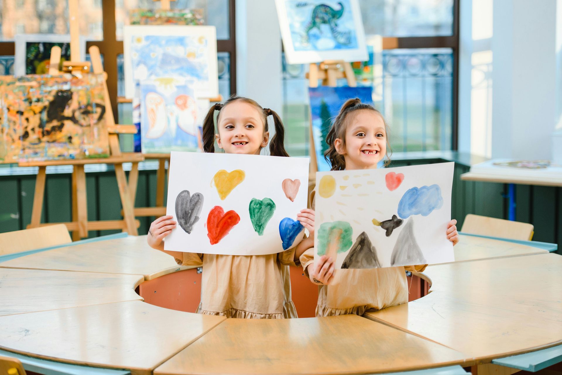 Two girls smiling, holding watercolor art in a classroom.
