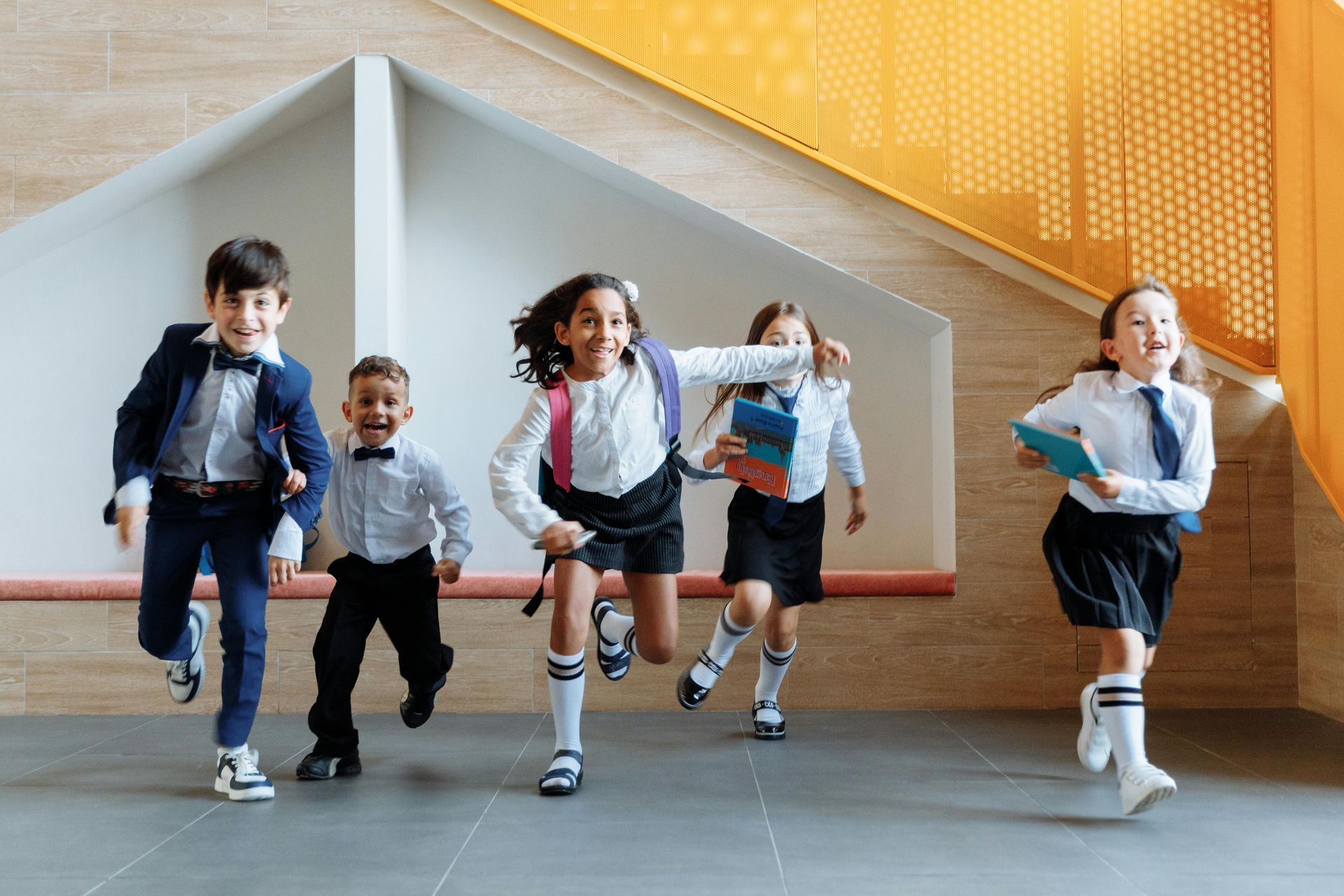 A group of children in school uniforms are running down a set of stairs.
