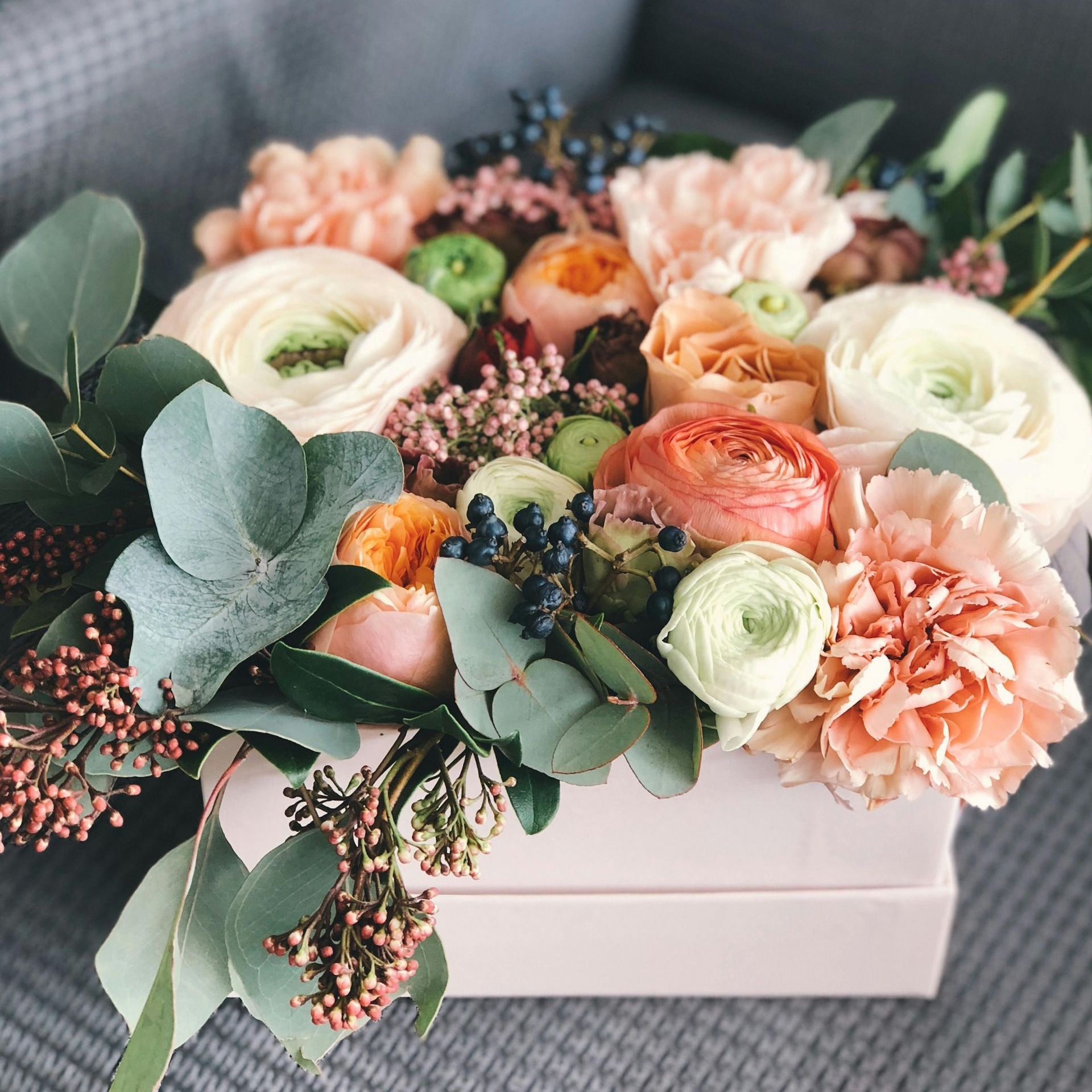 A box filled with flowers and leaves is sitting on a couch.