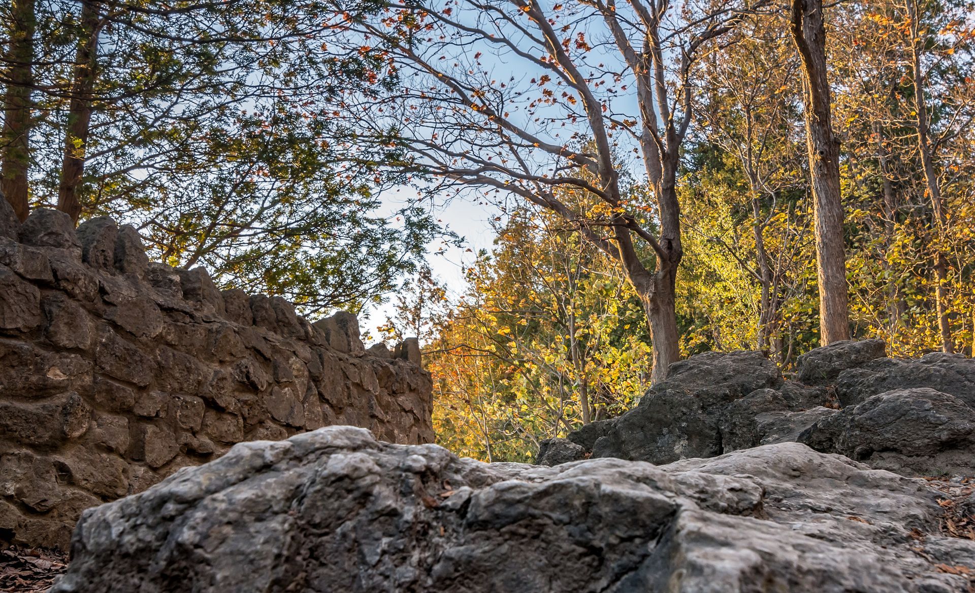 Rocky woodland trail with stone walls and sunlit autumn trees