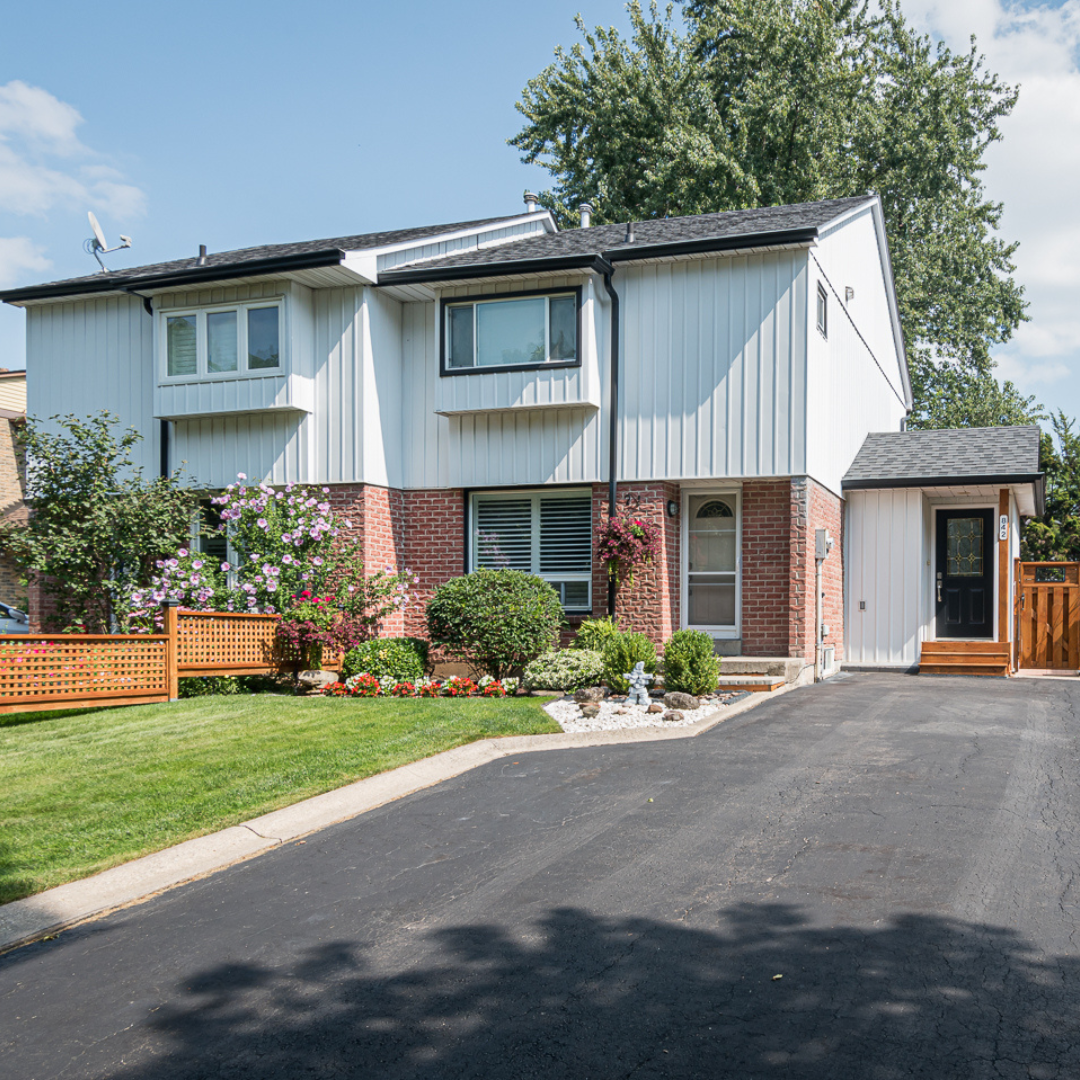 Suburban two-story house with driveway, lawn, brick accents, and a small front garden