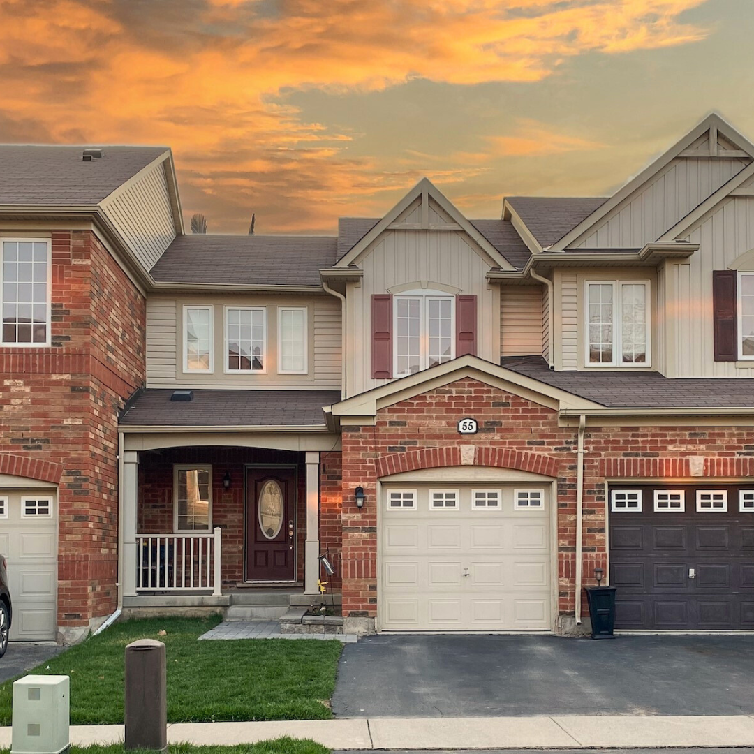 A brick house with two garage doors and a sunset in the background