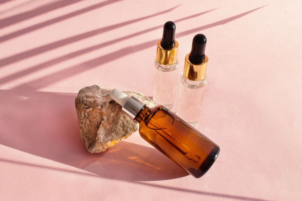 Amber perfume bottle with a stone, two small dropper bottles, on a pink background with soft shadows