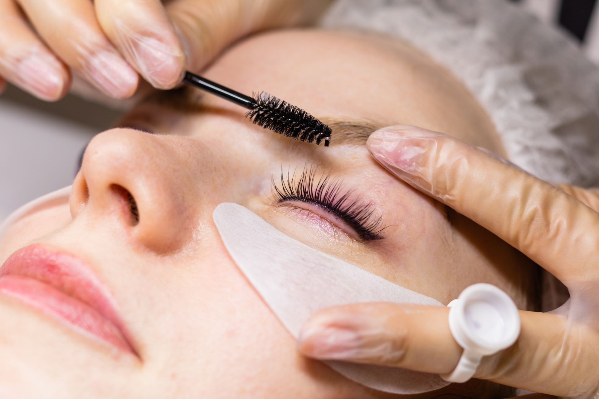 Beauty technician applying mascara to a closed eye with an eyelash pad in a spa treatment.