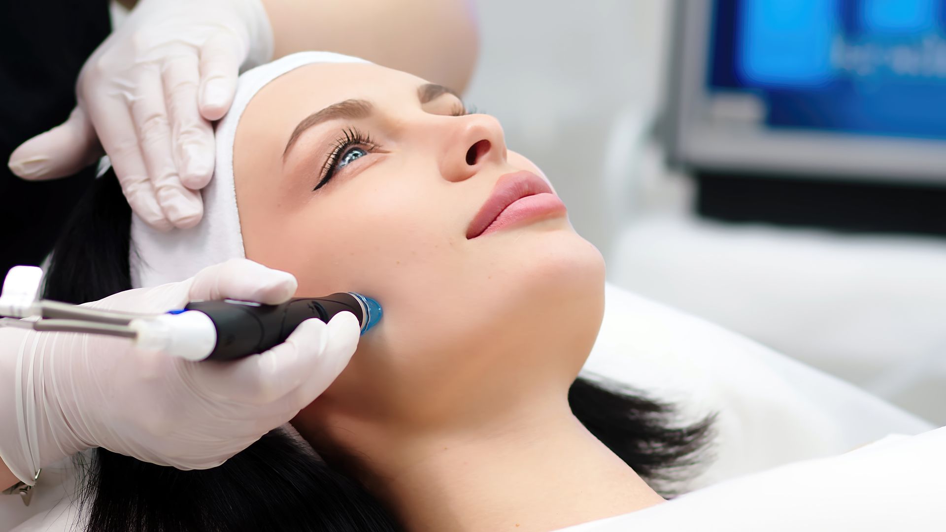 Cosmetic procedure on face with handheld device while client lies on treatment bed