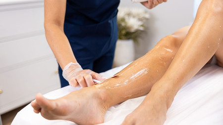 Massage therapist applying lotion to a person’s leg during a spa treatment