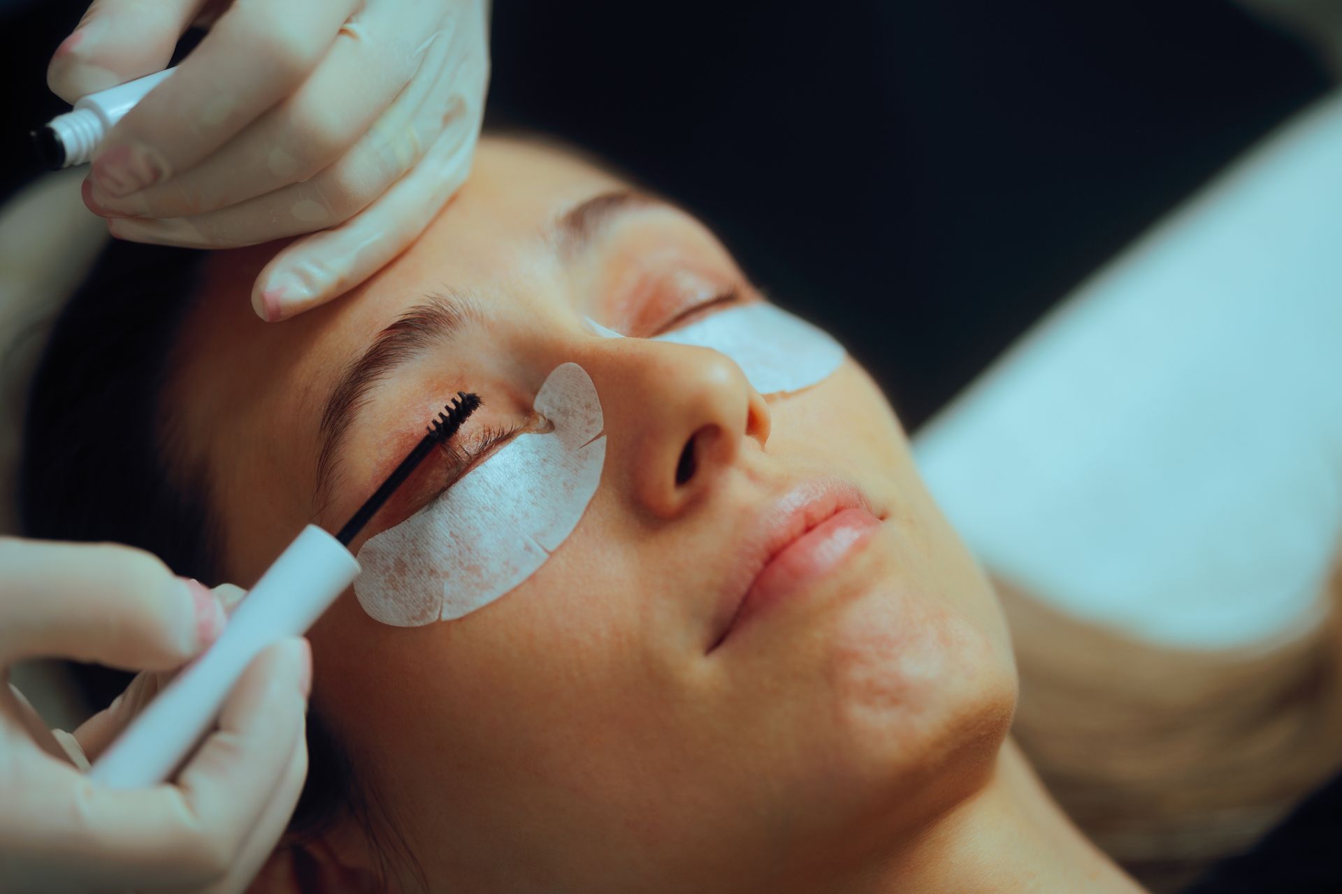 Spa technician applying under-eye patches to a client during a facial treatment
