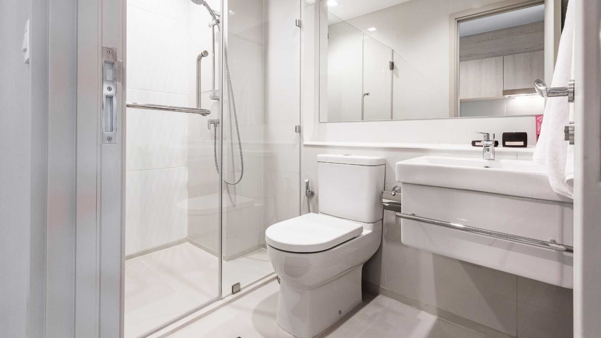 Modern white bathroom with glass shower, toilet, sink vanity, and large mirror