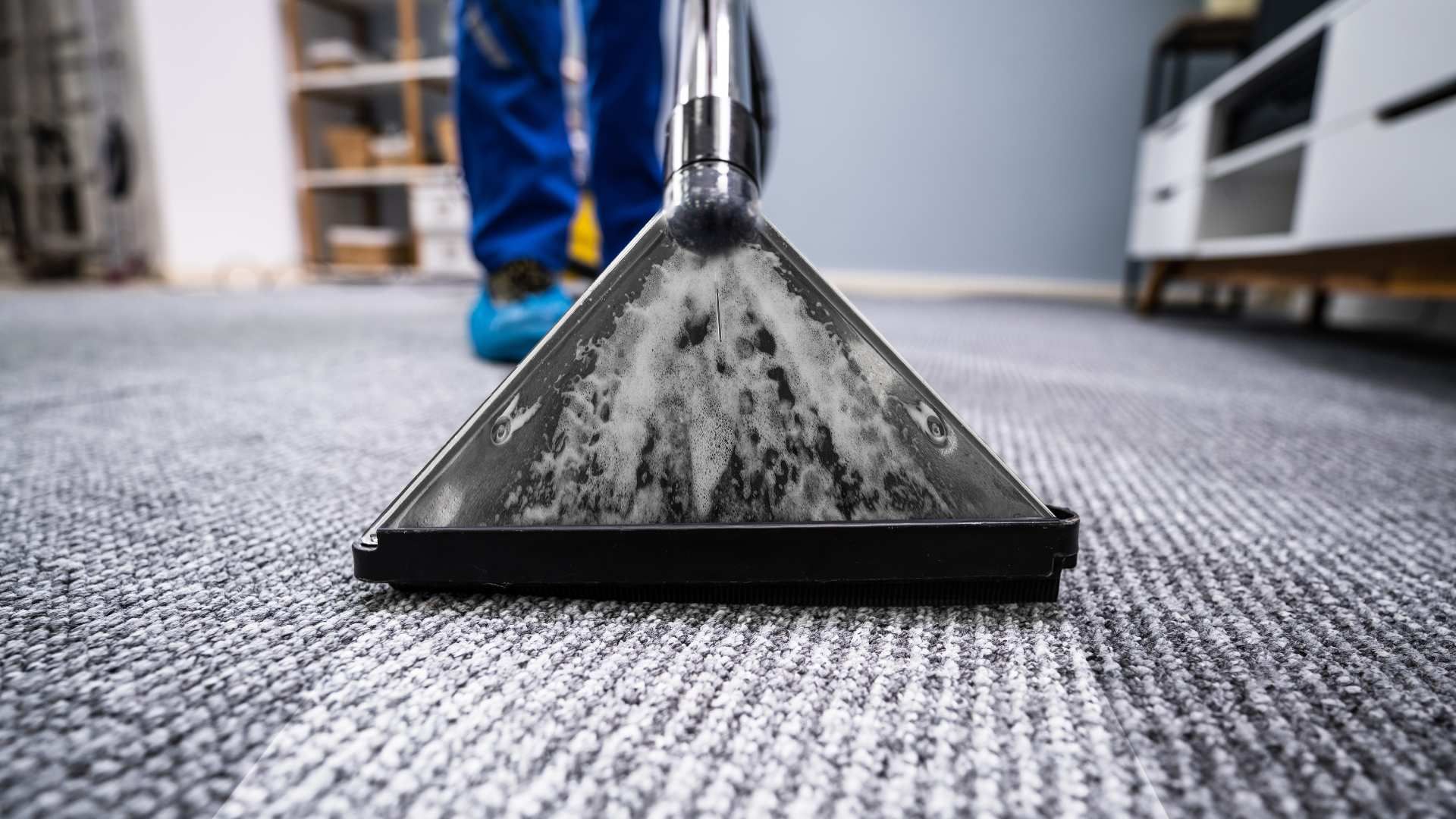 Carpet cleaner head vacuuming a gray rug in a room