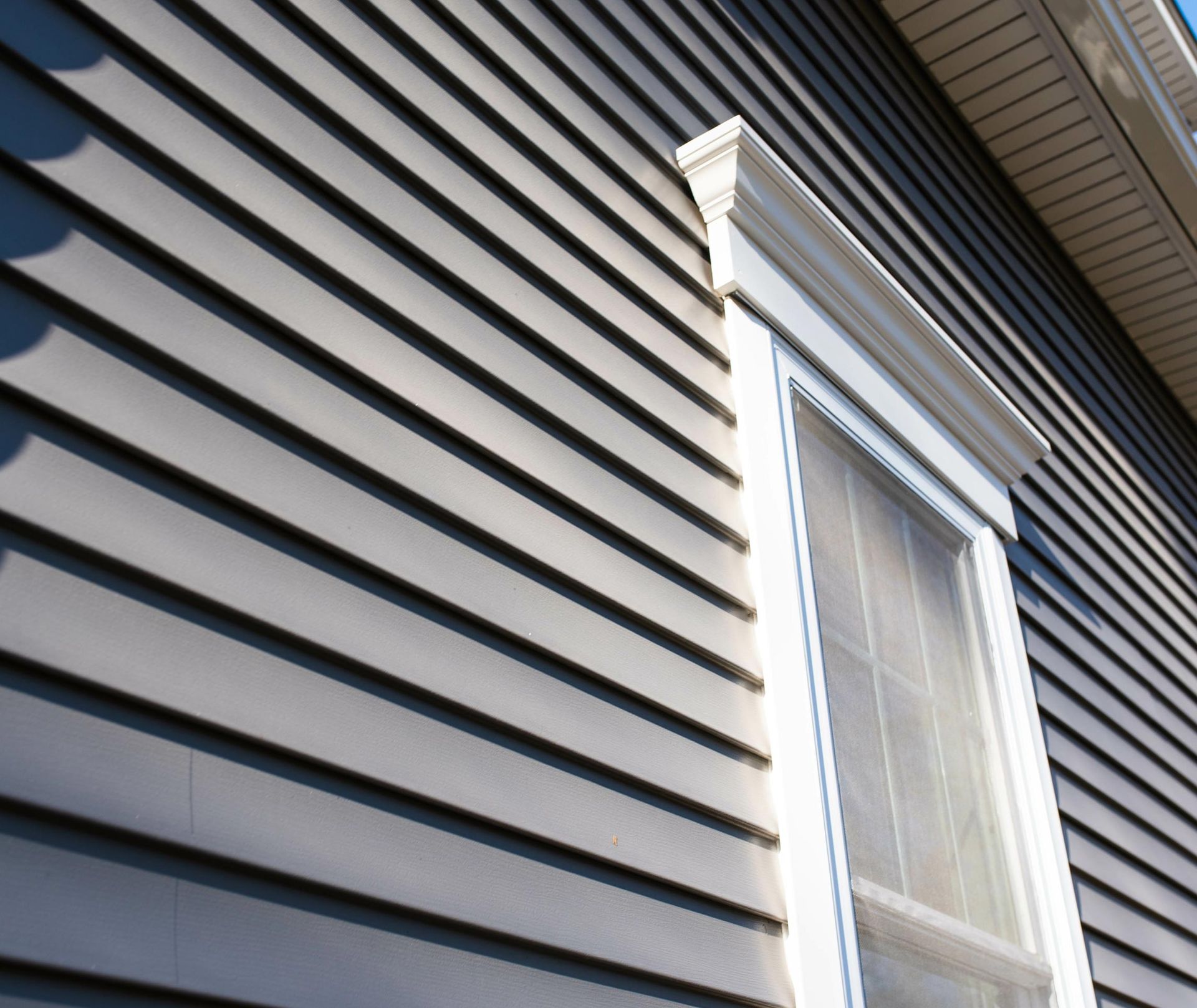 Close-up view of dark vinyl siding with a white-trimmed window on a house exterior.