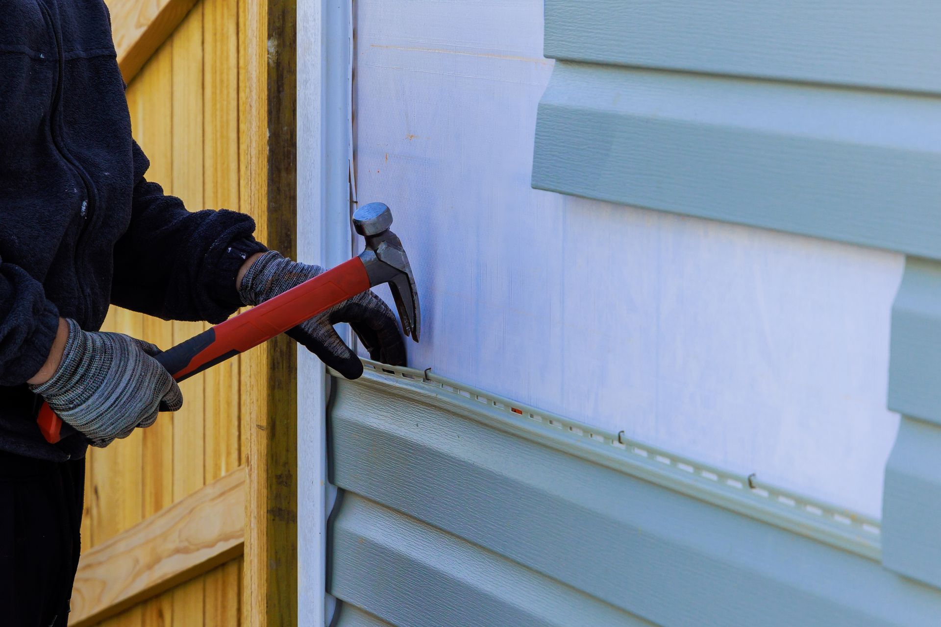 Contractor installing vinyl siding on a home exterior with a hammer.