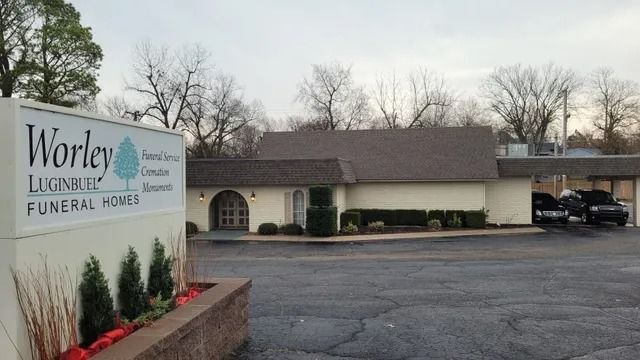 Worley Funeral Home sign beside a beige building and parking lot under overcast trees