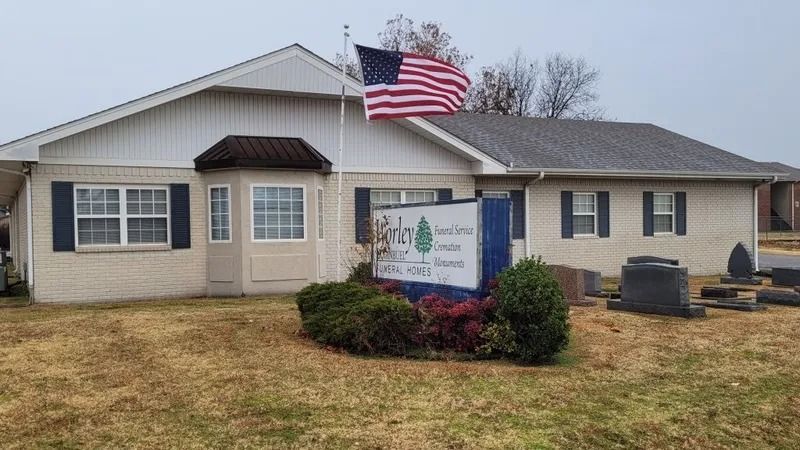 Small beige community building with an American flag and a sign in front, on a cloudy day