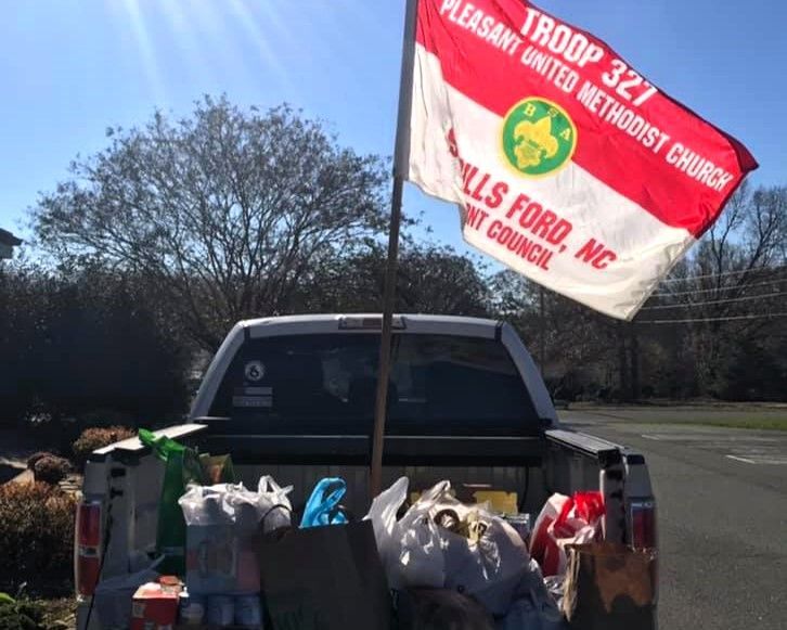 Truck bed filled with donation bags beside a red-and-white Boy Scouts troop banner outdoors
