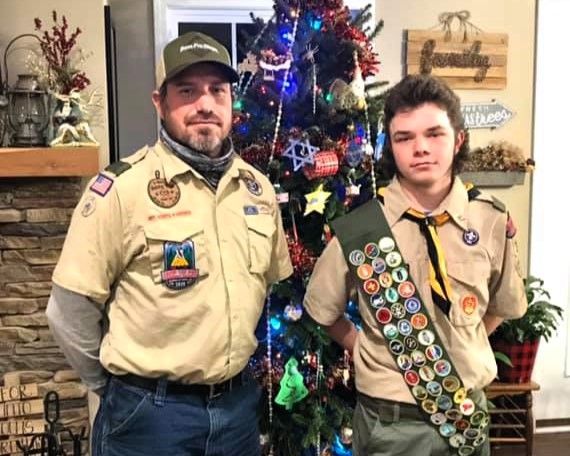 Two scouts in tan uniforms pose in front of a decorated Christmas tree.