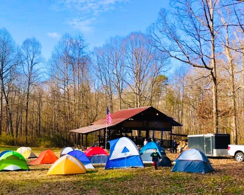 Campsite with colorful tents in front of a rustic cabin in a leafless wooded area under a clear blue sky