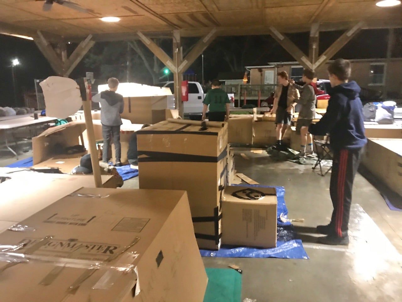 People loading boxes and furniture on blue tarps in a covered warehouse-like space.