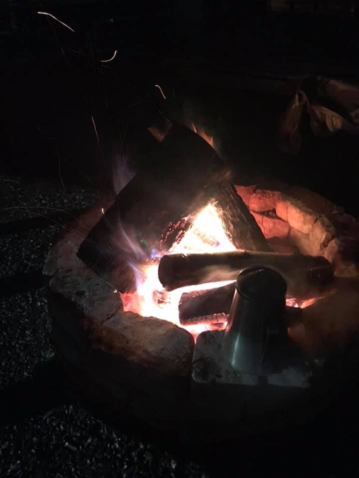 Campfire burning in a stone fire pit at night, with glowing logs and a dark outdoor setting.