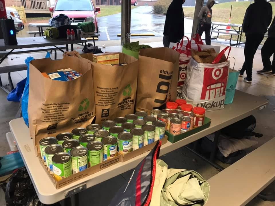 Charity table with canned goods, paper grocery bags, and Target bags under a tent
