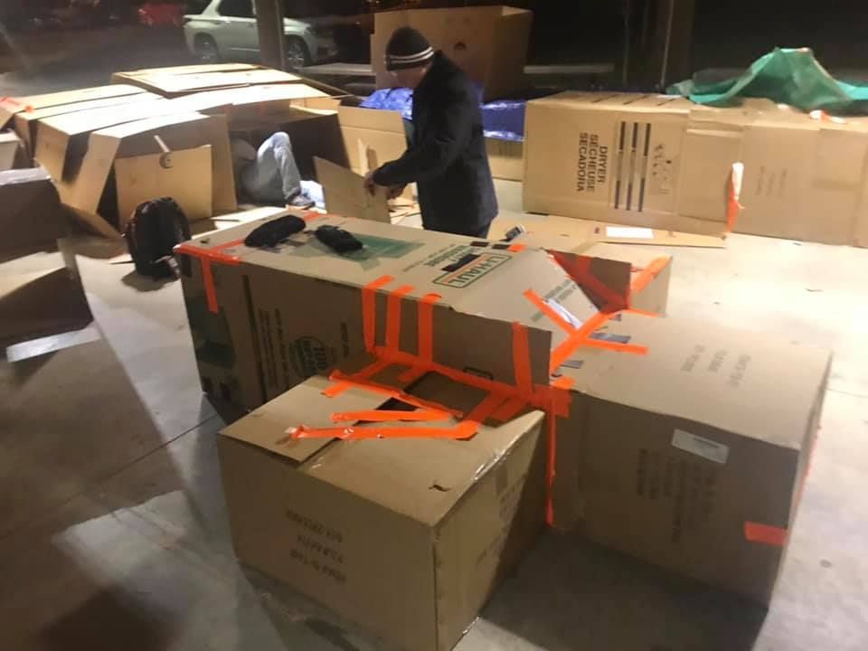 Person in blue jacket moving among stacked cardboard boxes in a warehouse.