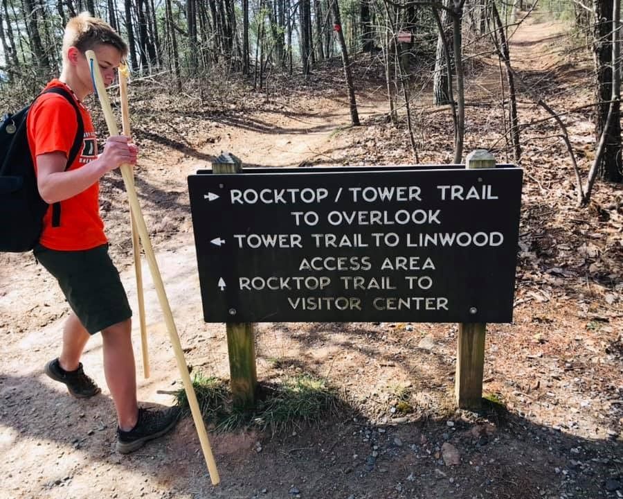 Hiker beside trail sign for Rocktop/Tower Trail and overlooks in a wooded area