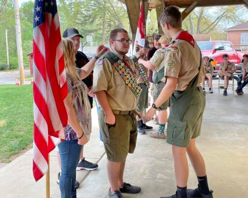 Boy Scouts talking under a pavilion beside an American flag.