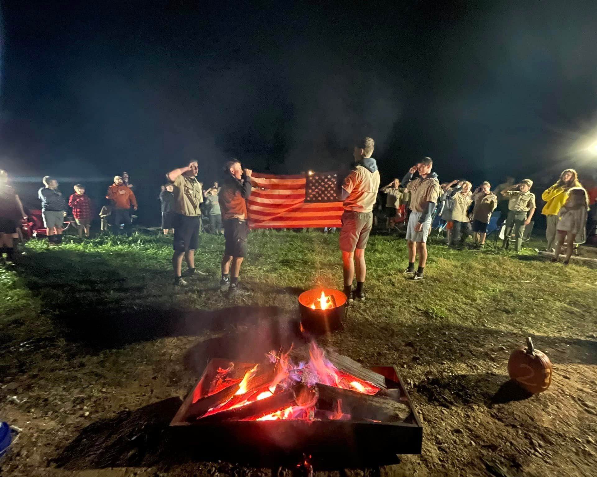 People holding an American flag at a nighttime campfire gathering outdoors