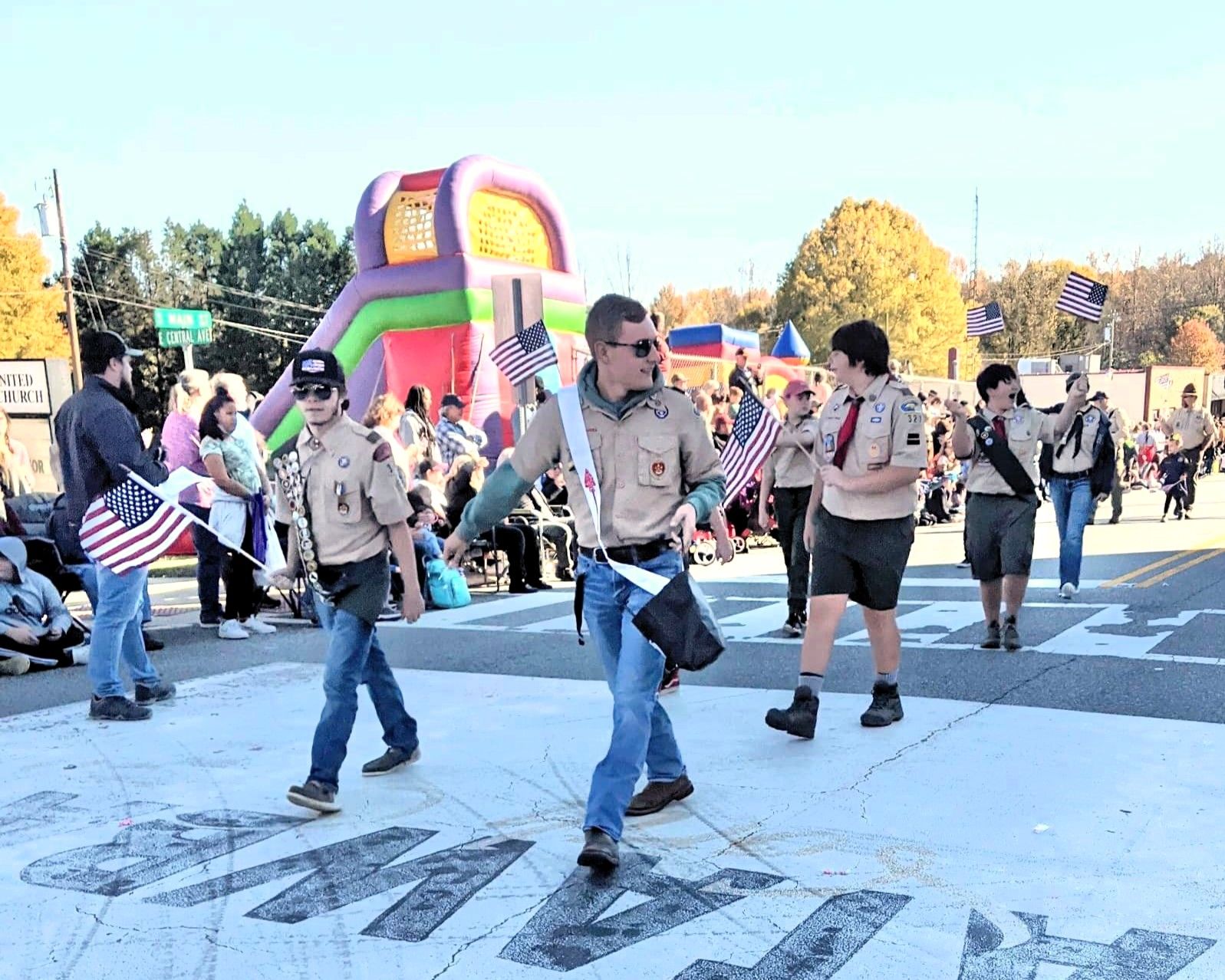 People dancing in uniform shirts at an outdoor street parade with an inflatable bounce house in the background