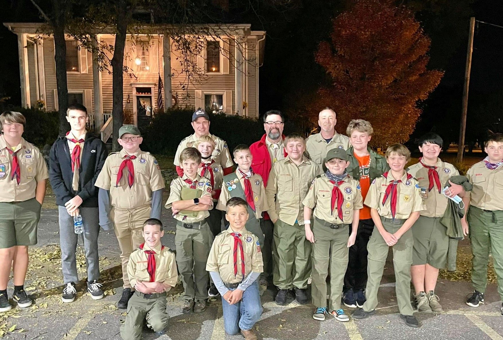 Group of scouts in uniform posing outside a building at night.