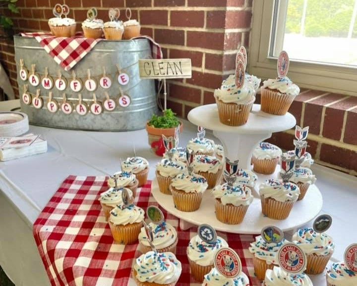 Cupcake display on a dessert table with red checkered cloth, white stands, and a brick wall backdrop