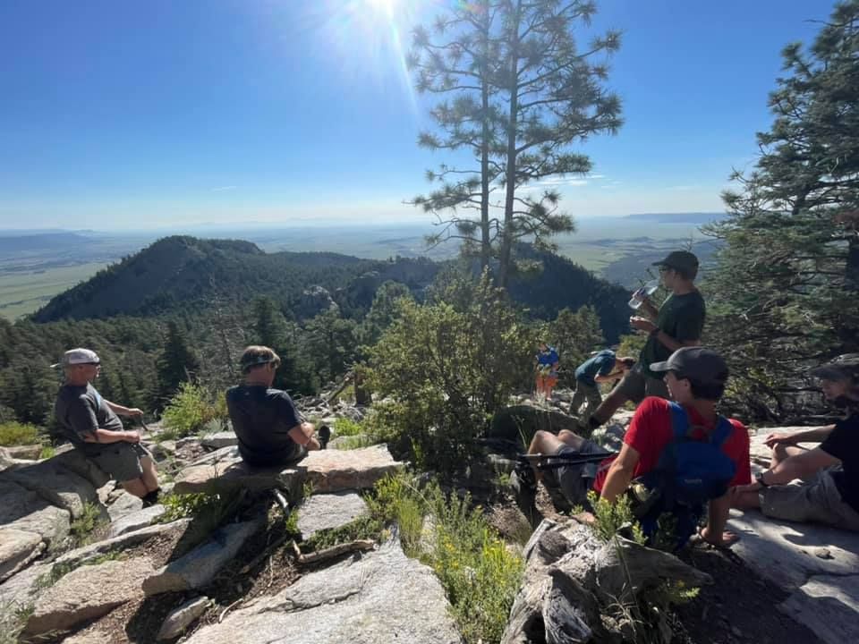 Hikers resting on rocks atop a sunny mountain overlook with backpacks and a sweeping valley view