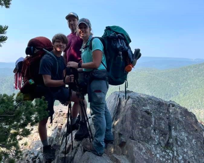 Four hikers with backpacks standing on a rocky mountain overlook above a forested valley