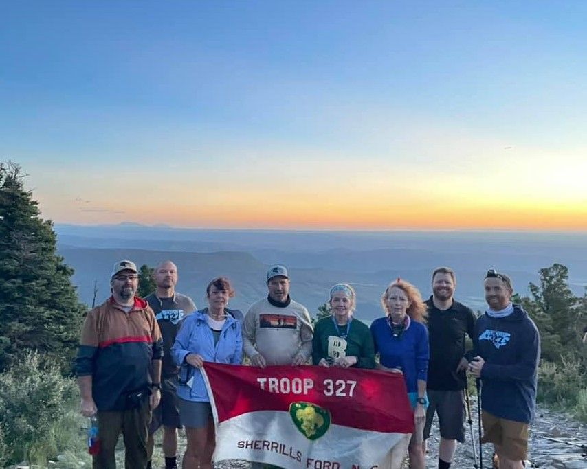 Group of hikers holding a Troop 327 banner at sunrise on a mountain overlook